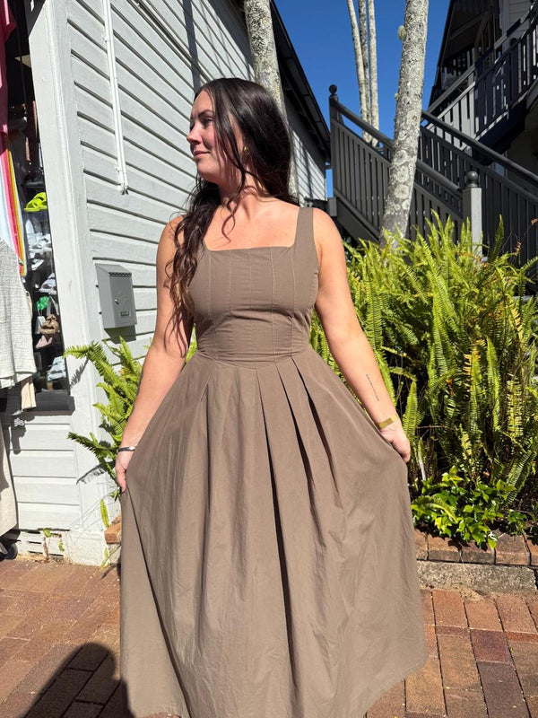 Woman wearing a brown dress standing outdoors on a sunny day.