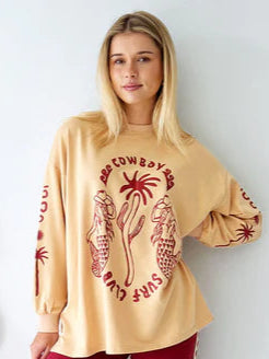 Woman wearing a beige long-sleeve top with a graphic design and red pants against a white background