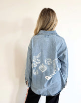 Person wearing a blue denim jacket with white designs on the back against a plain background